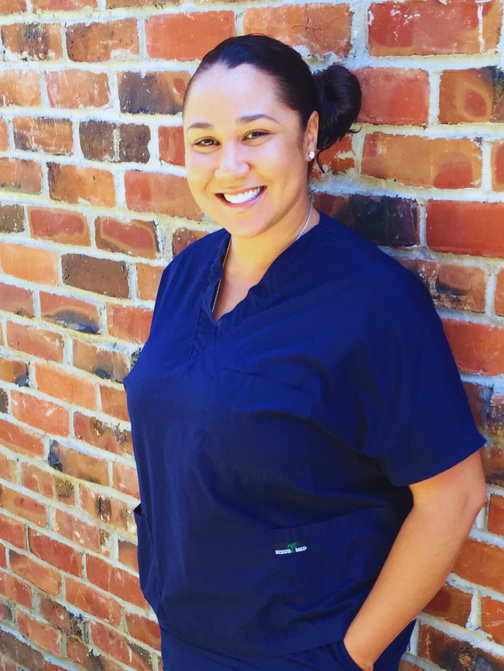 Colette smiling  in scrubs standing in front of a brick wall